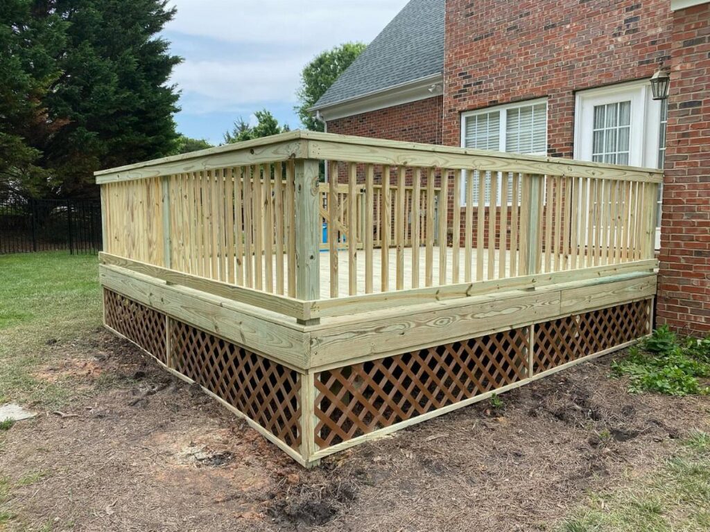 Raised wooden deck with brown diamond lattice skirting attached to a red brick house.