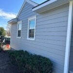 Light blue horizontal siding on a house with white window trim and green bushes below.