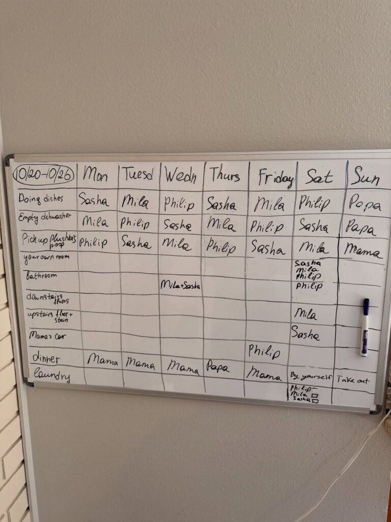 Handwritten weekly chore chart on a white dry-erase board with assigned names.