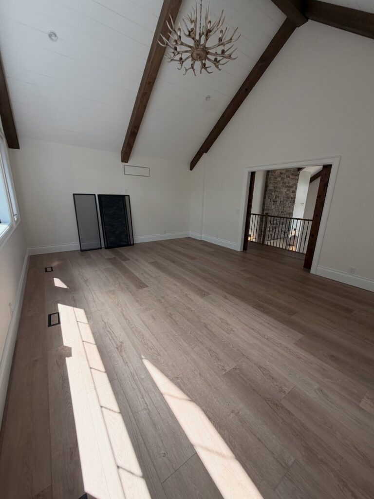 Light wood-look luxury vinyl plank flooring in an empty room with white walls and dark ceiling beams.