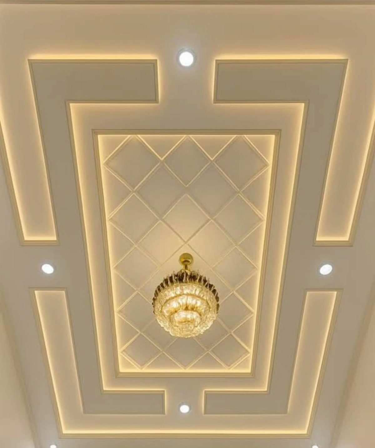 White tiered recessed ceiling with geometric LED lighting and a gold crystal chandelier.
