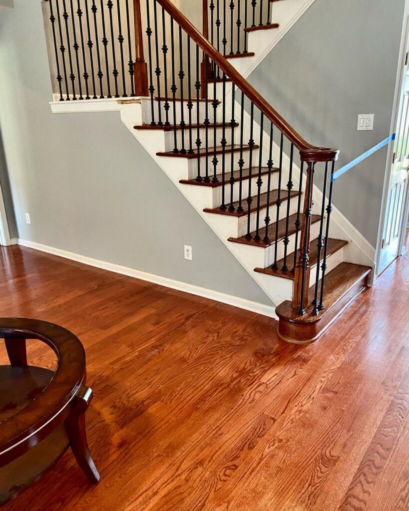 Reddish medium hardwood floors in a room next to a wooden staircase with black spindles.