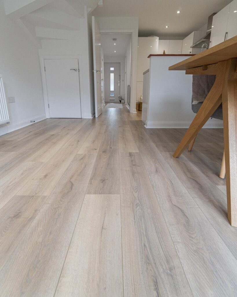 Light wood-look laminate flooring stretching through a bright modern home hallway and kitchen.