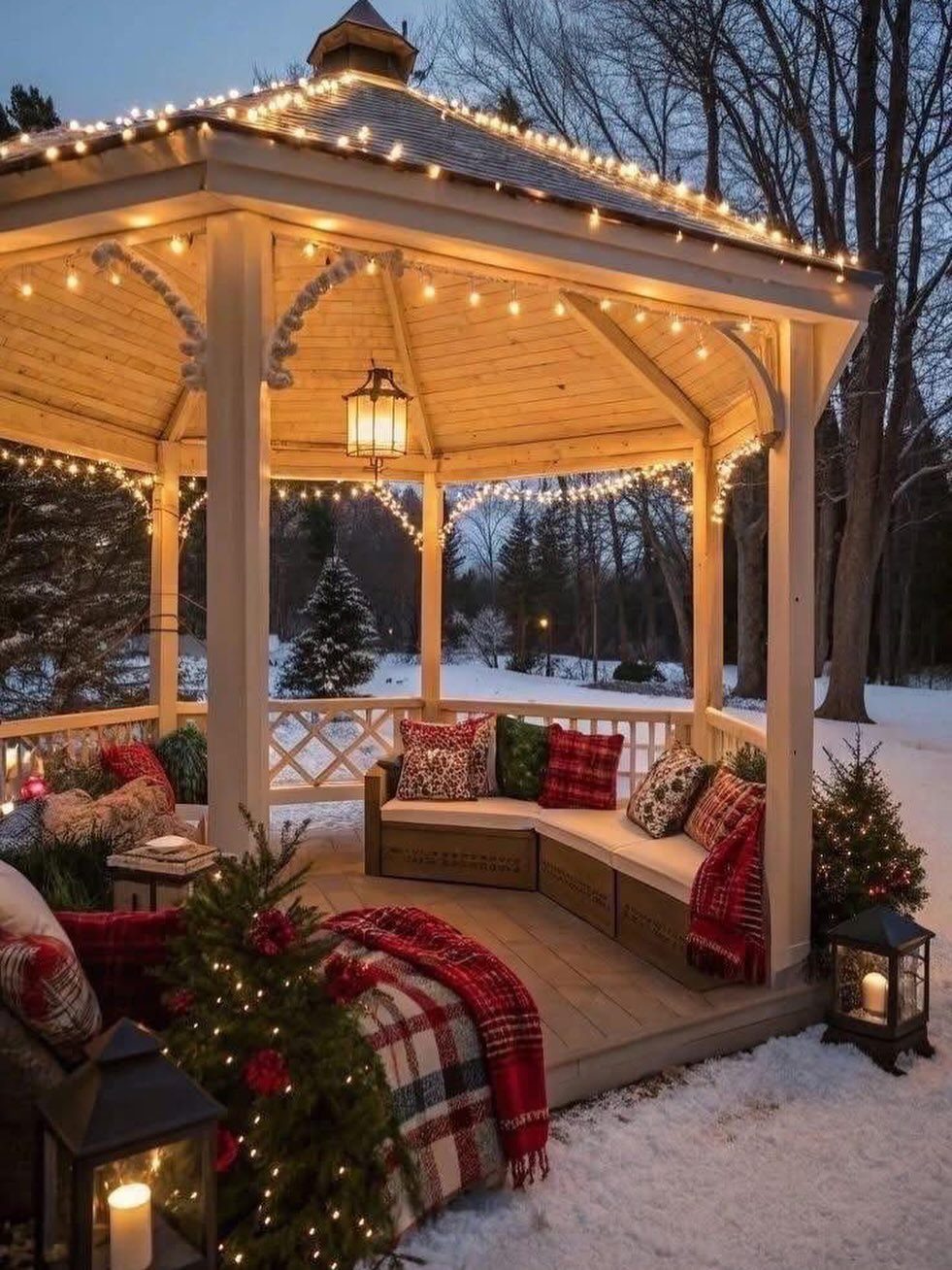 White wooden gazebo decorated with warm string lights and cozy pillows in winter snow.