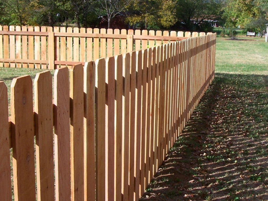 Natural wood picket fence bordering a grassy yard and a dirt path.