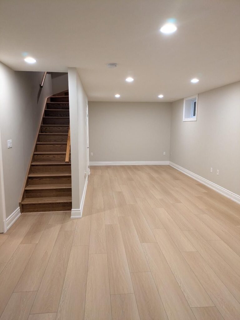 Light sandy taupe vinyl plank flooring in an empty room with a wooden staircase.