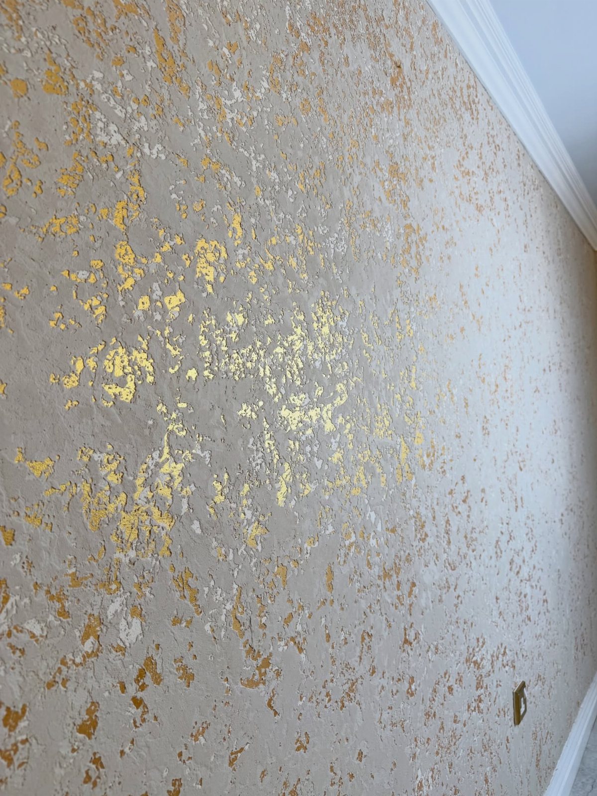 Textured beige wall with irregular gold metallic accents scattered across the surface.